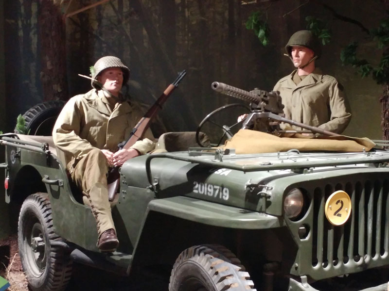 Two mannequin soldiers in roofless vehicle.